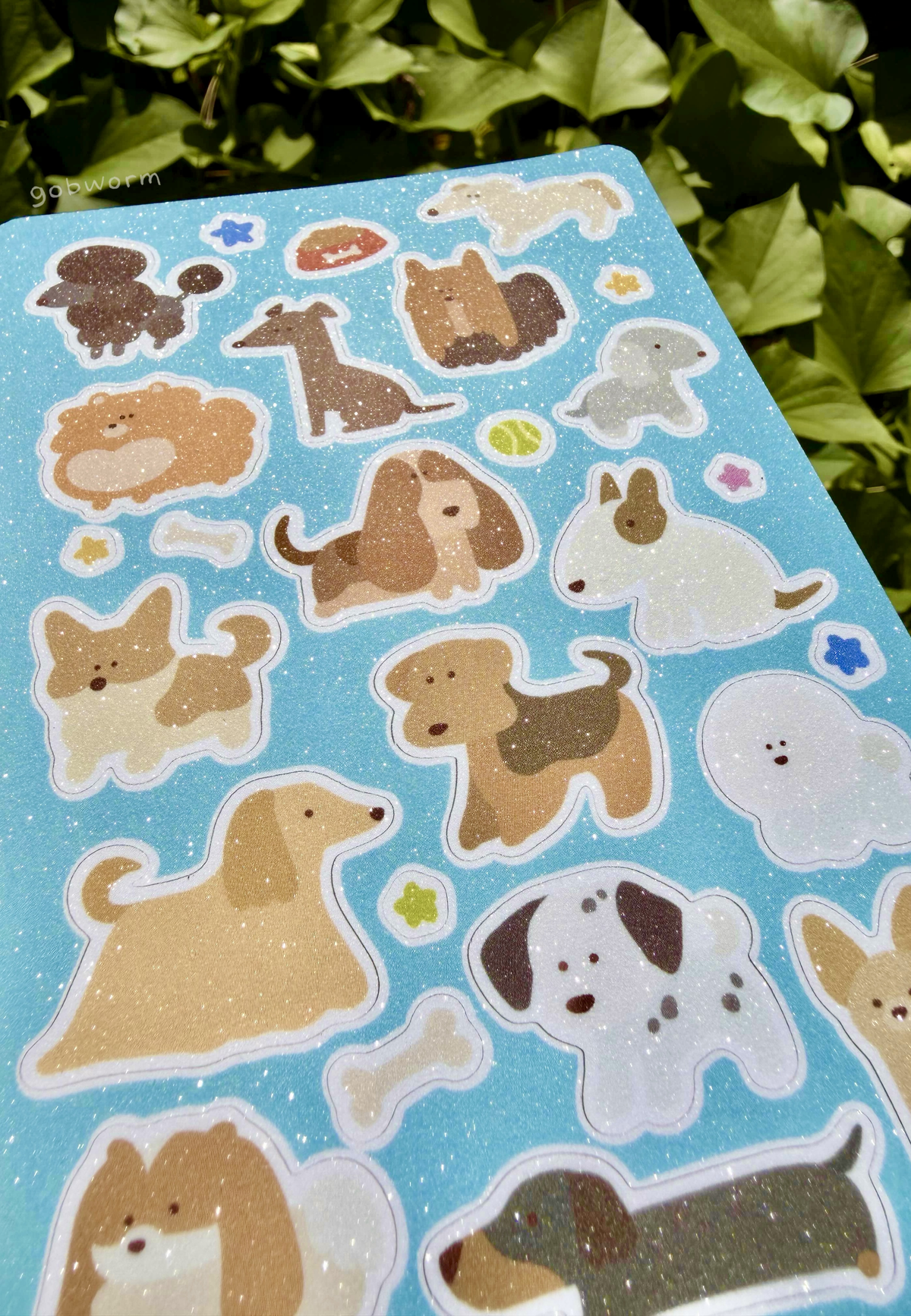 close up of sticker sheet featuring lineless illustrations of various dog breeds with a light blue background and glittery finish