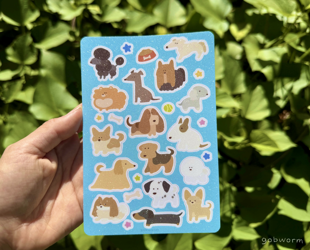 hand holding a sticker sheet featuring lineless illustrations of various dog breeds with a light blue background and glittery finish
