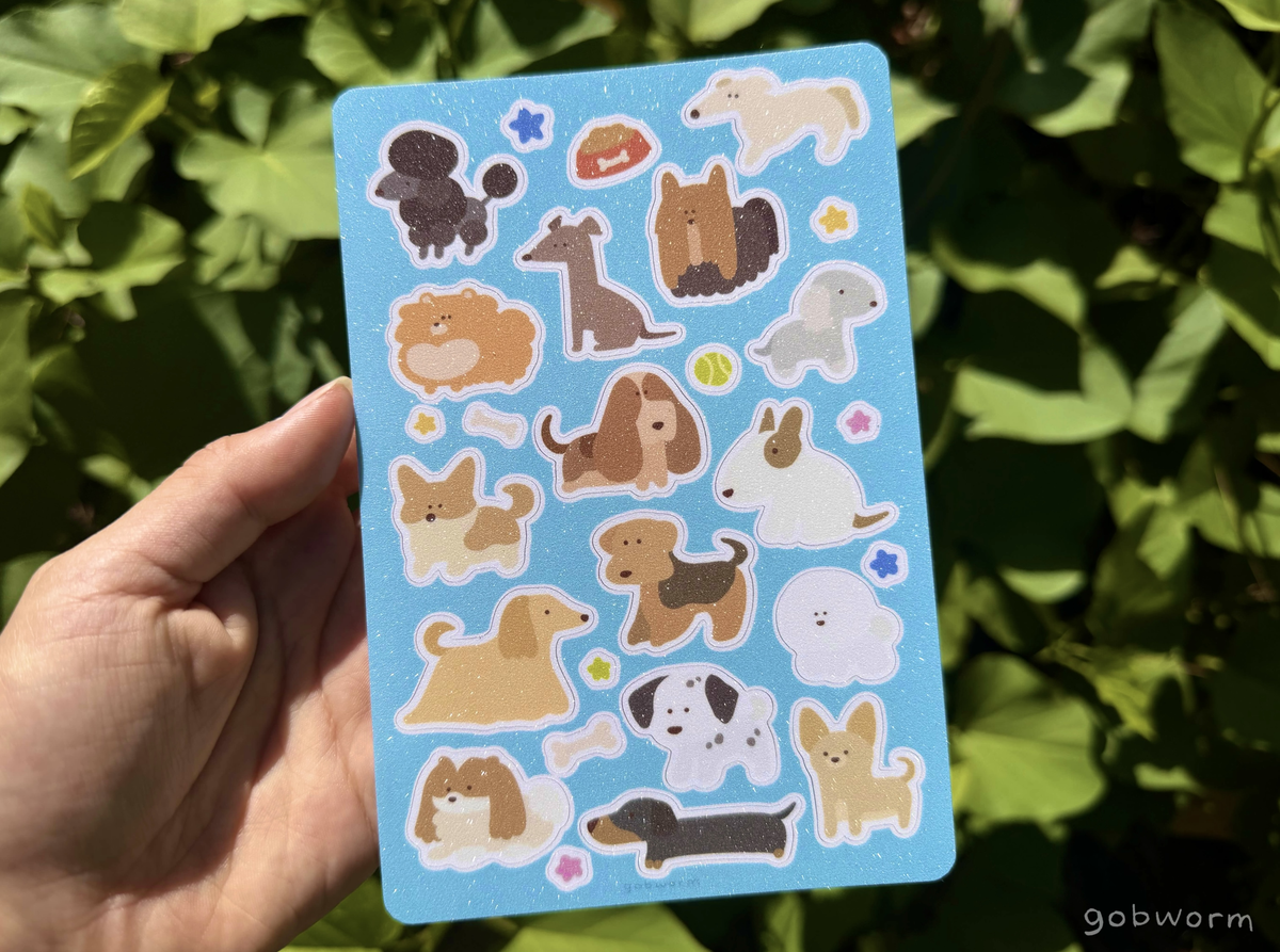 hand holding a sticker sheet featuring lineless illustrations of various dog breeds with a light blue background and glittery finish